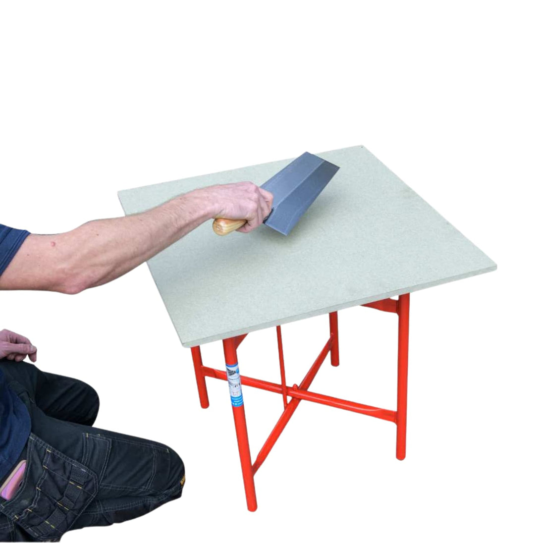 Man kneeling down using a hand tool on a red plastering table.