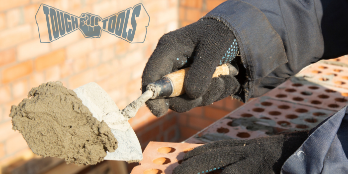 Mans hands holding a brick and using a trowel to apply mortar